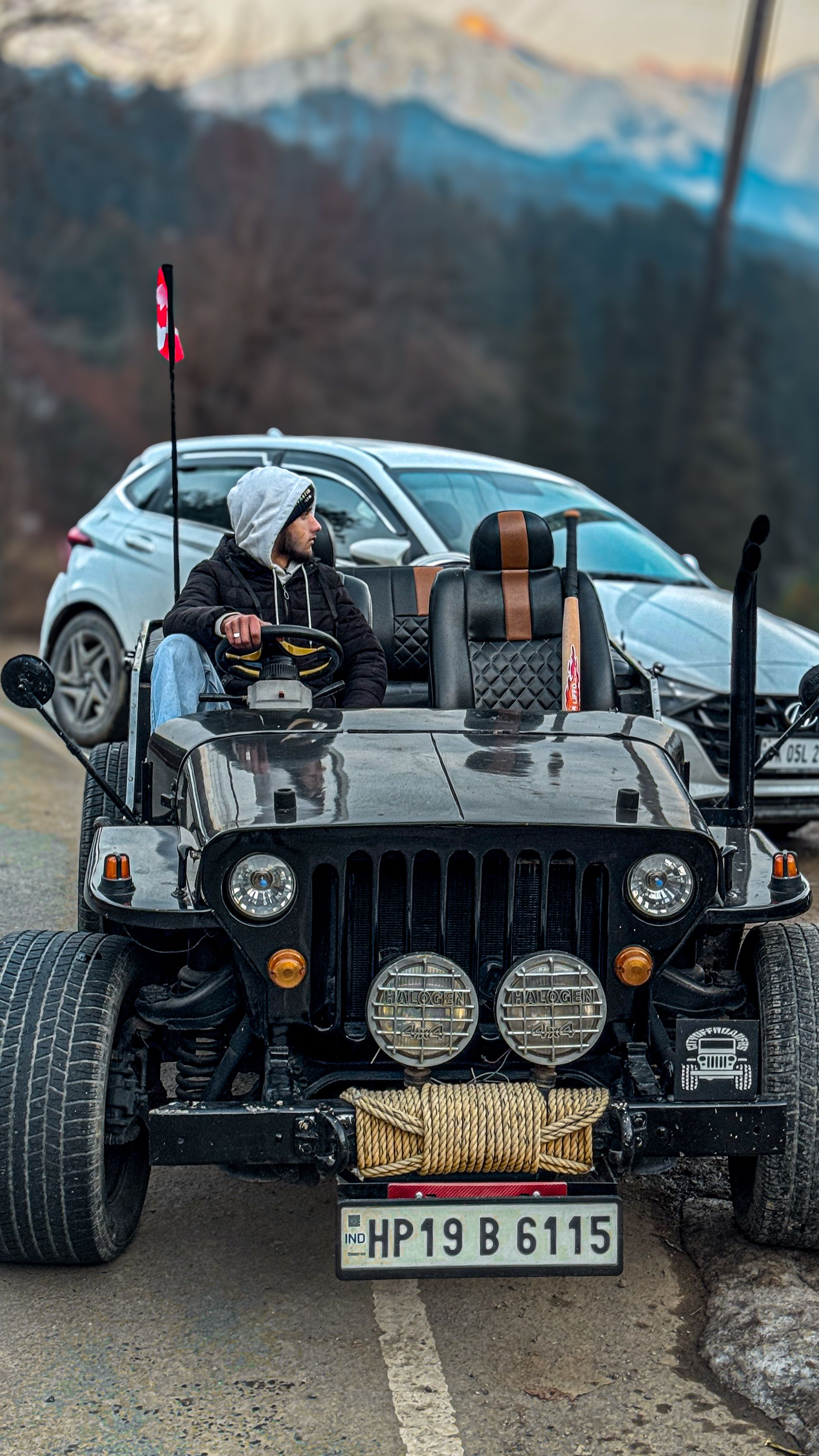 Man driving a modified jeep on a mountain road, captured during the day.