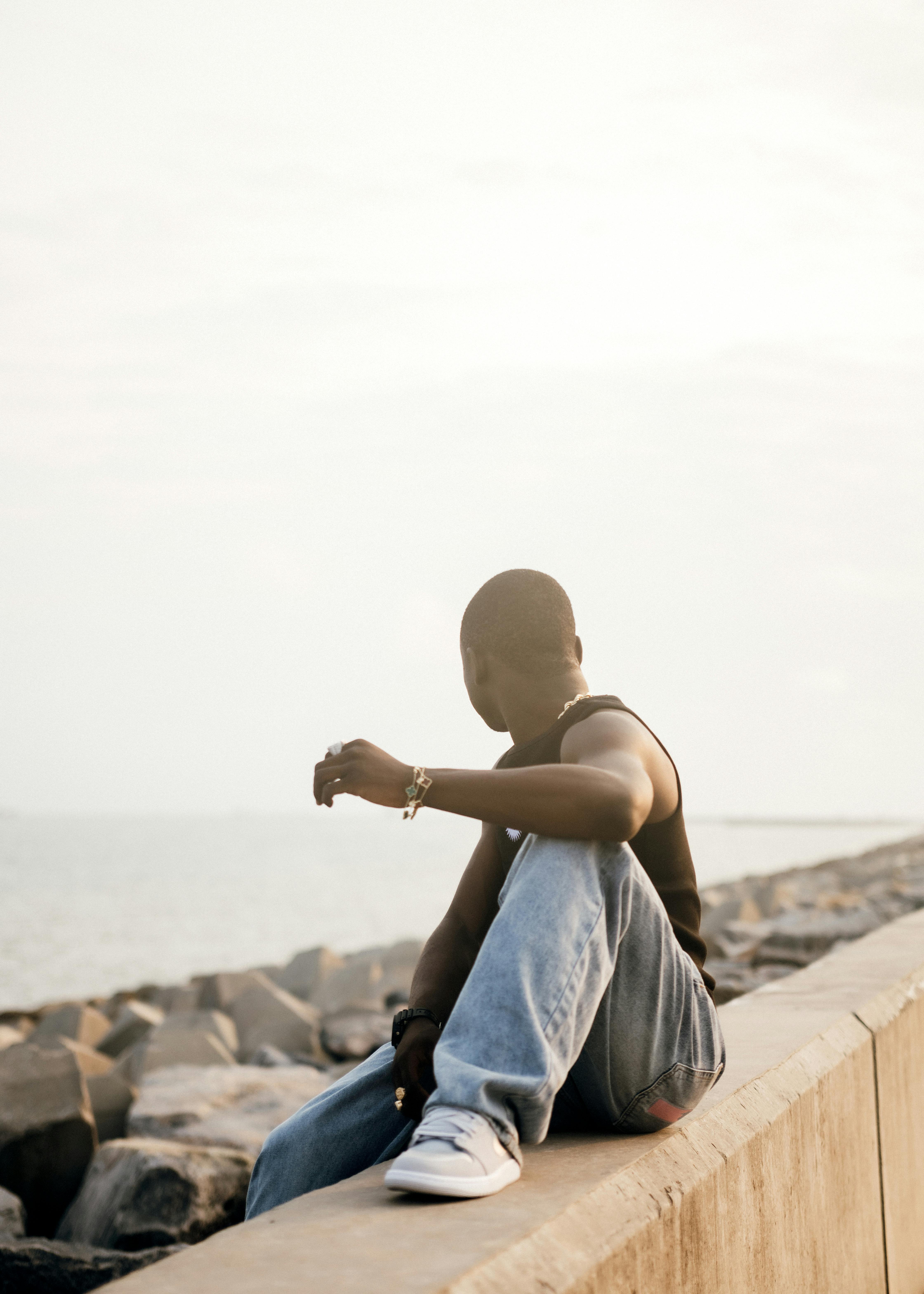 A man sitting pensively by the ocean on a sunny day.