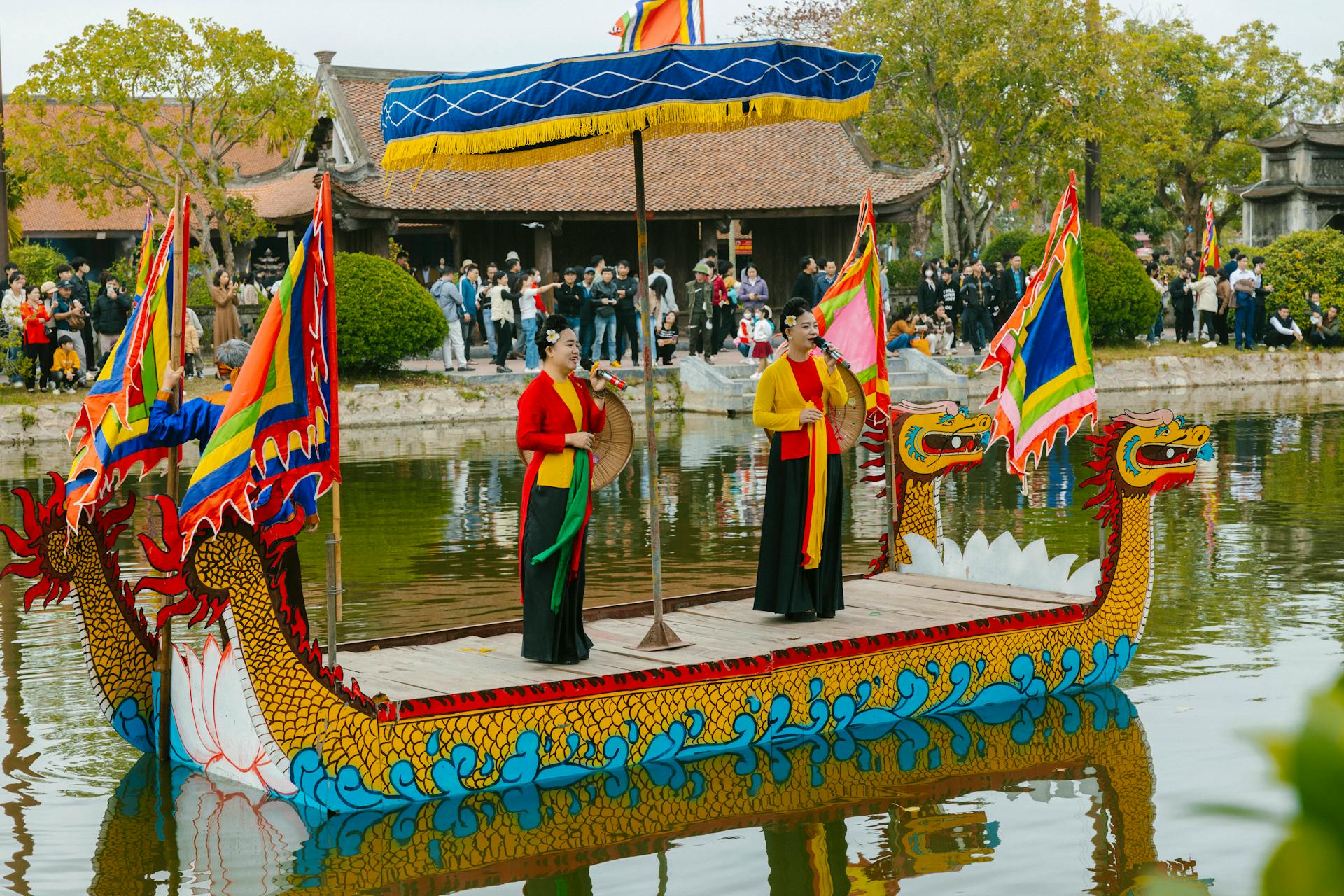 Vibrant dragon boat with performers and flags on a scenic lake, cultural festival vibe.