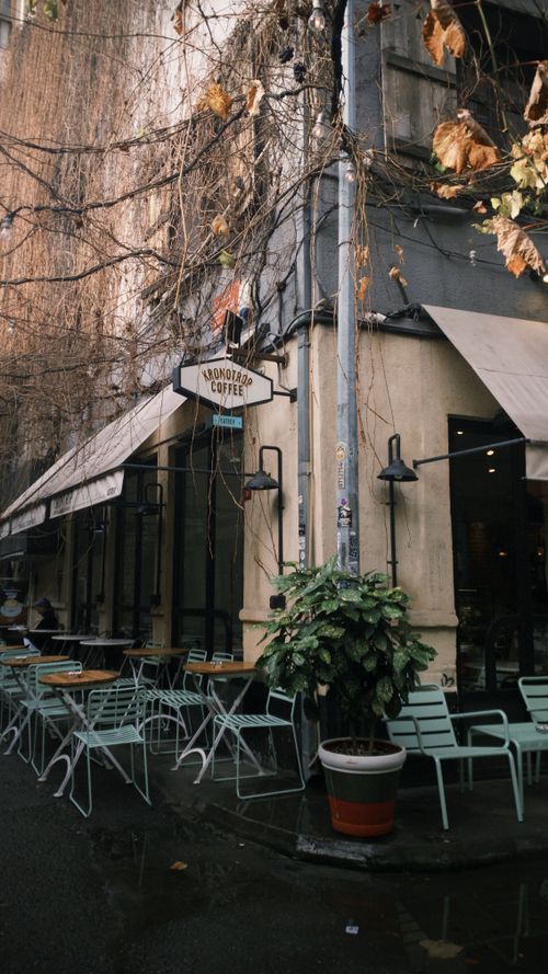 Free A charming outdoor cafe on a quiet street corner with empty seating and autumn leaves. Stock Photo