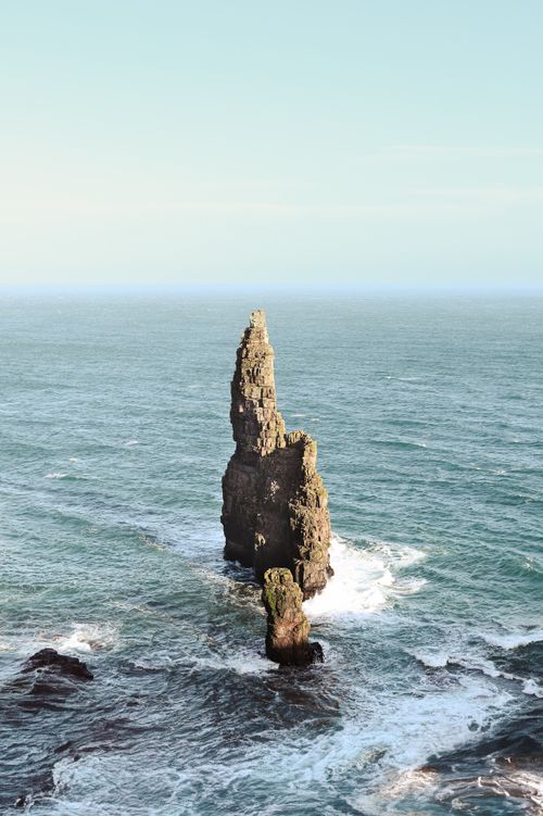 Free A stunning sea stack rises dramatically from the ocean waves in serene daylight. Stock Photo