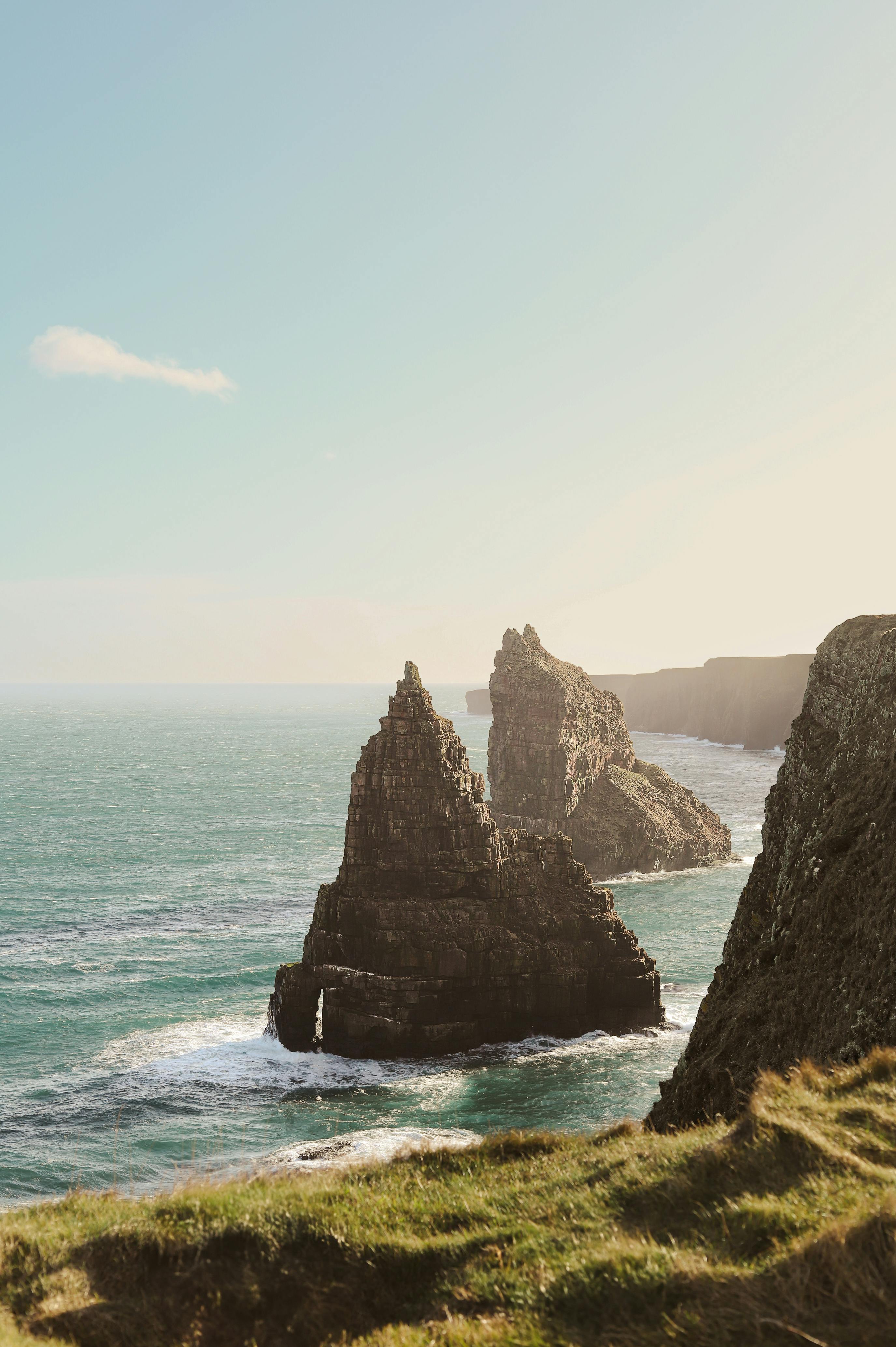 Scenic view of towering rock formations along a rugged coastline under a clear sky.