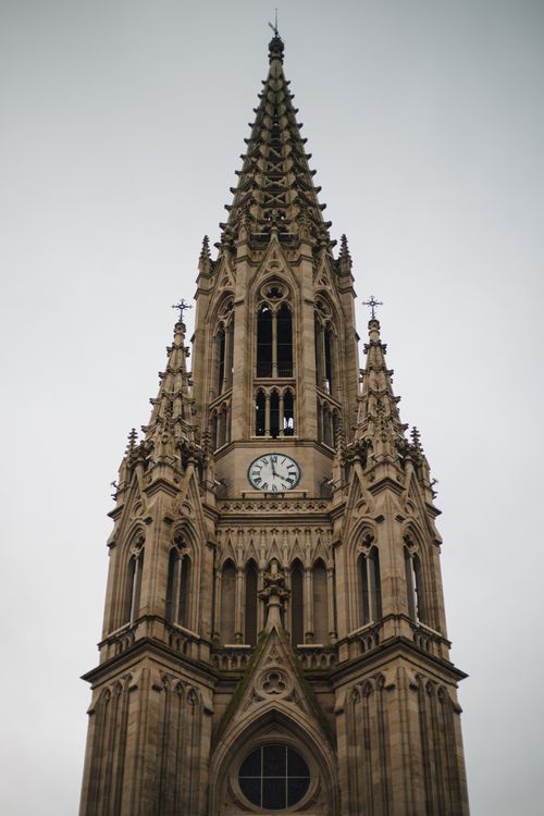 Free Majestic gothic cathedral tower featuring an ornate clock under cloudy skies. Stock Photo