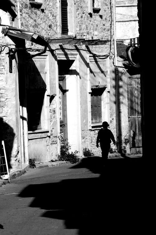 Free A person walks in silhouette through a historic, shadow-filled alleyway in black and white. Stock Photo