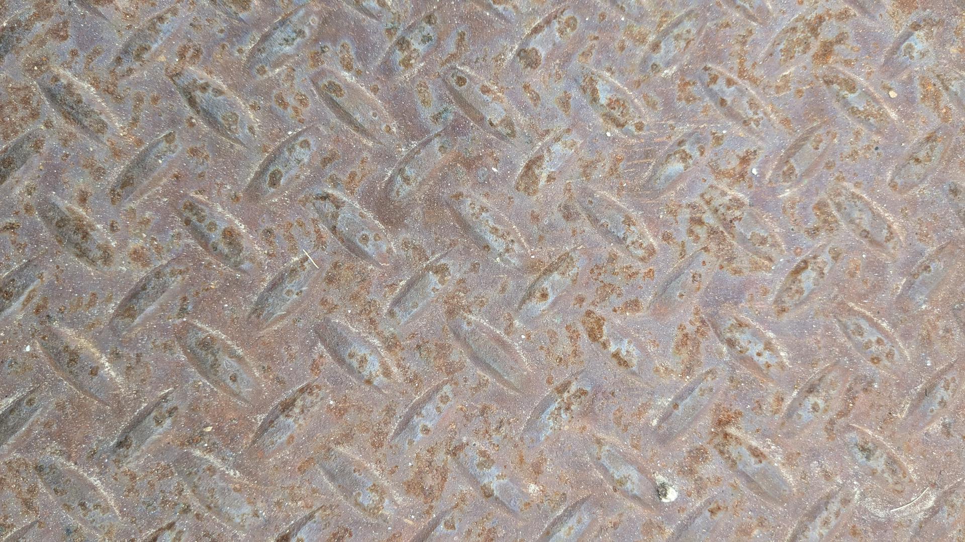 Detailed view of a rusty metal diamond plate, showcasing its textured pattern and weathered surface.