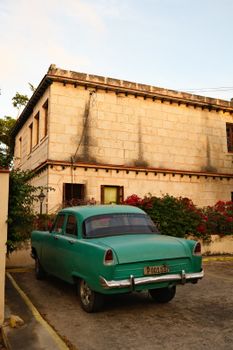 Classic green car parked by a stone building, conveying a vintage and timeless feel.