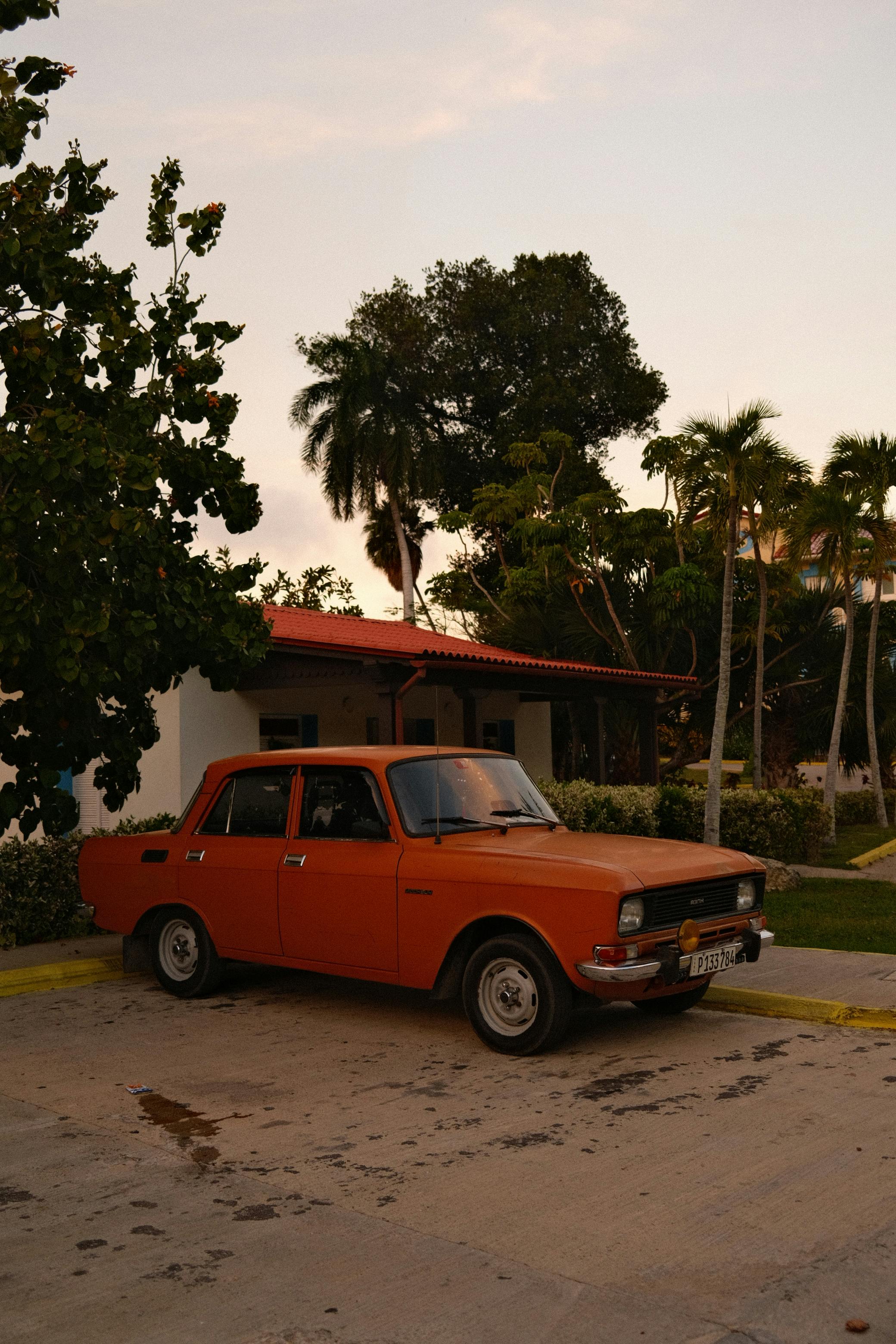 vintage orange car parked by tropical house