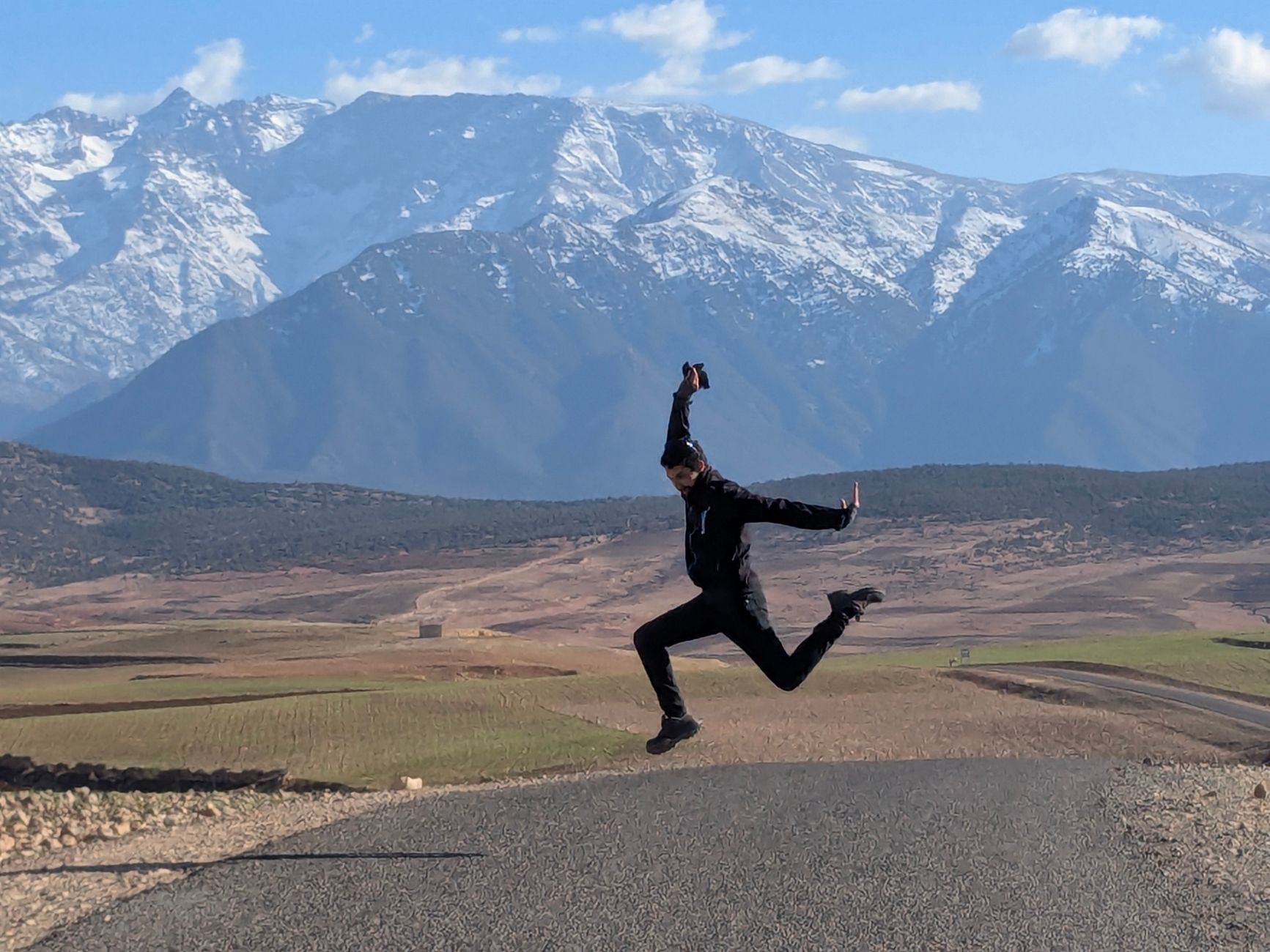 A joyful moment captured as a person leaps on an open road with stunning mountain views in the background.