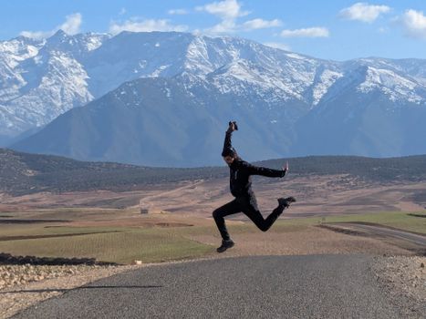 A joyful moment captured as a person leaps on an open road with stunning mountain views in the background.