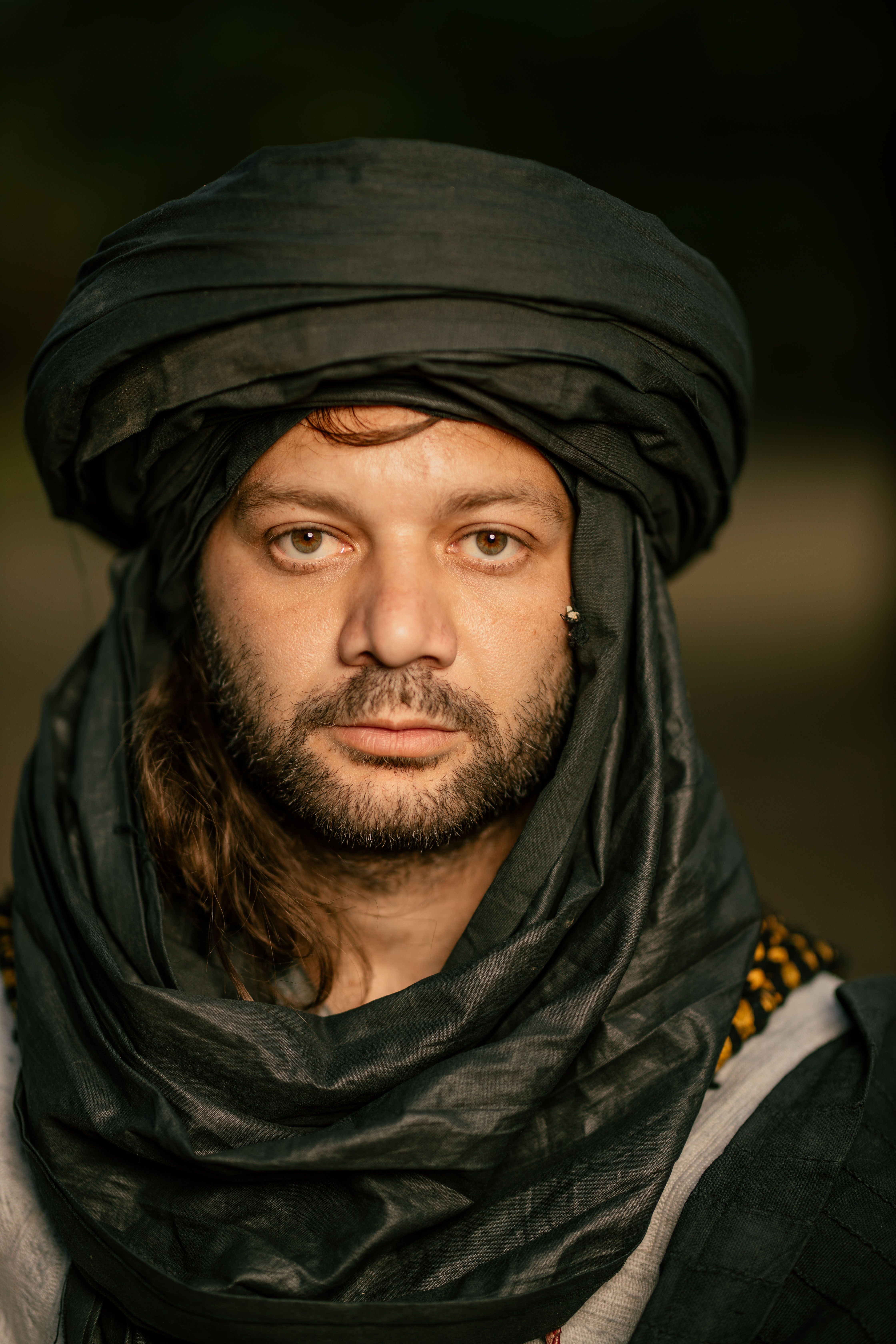 Close-up portrait of a man wearing traditional headwear, set outdoors in soft light.