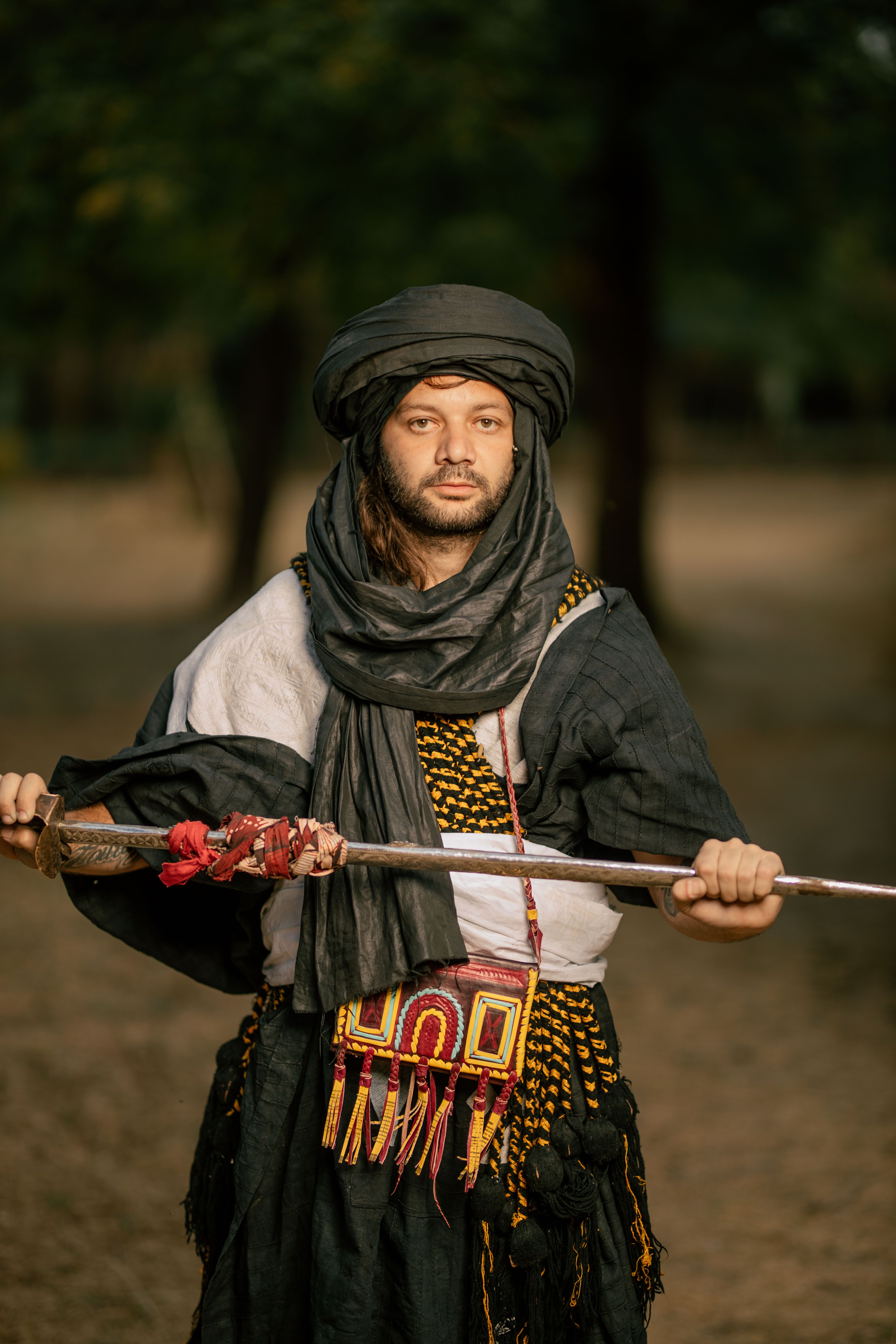 A nomadic man in traditional attire holding a spear in an arid outdoor setting.