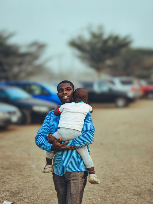 Free A father carries his child in an outdoor parking area on a calm day. Stock Photo