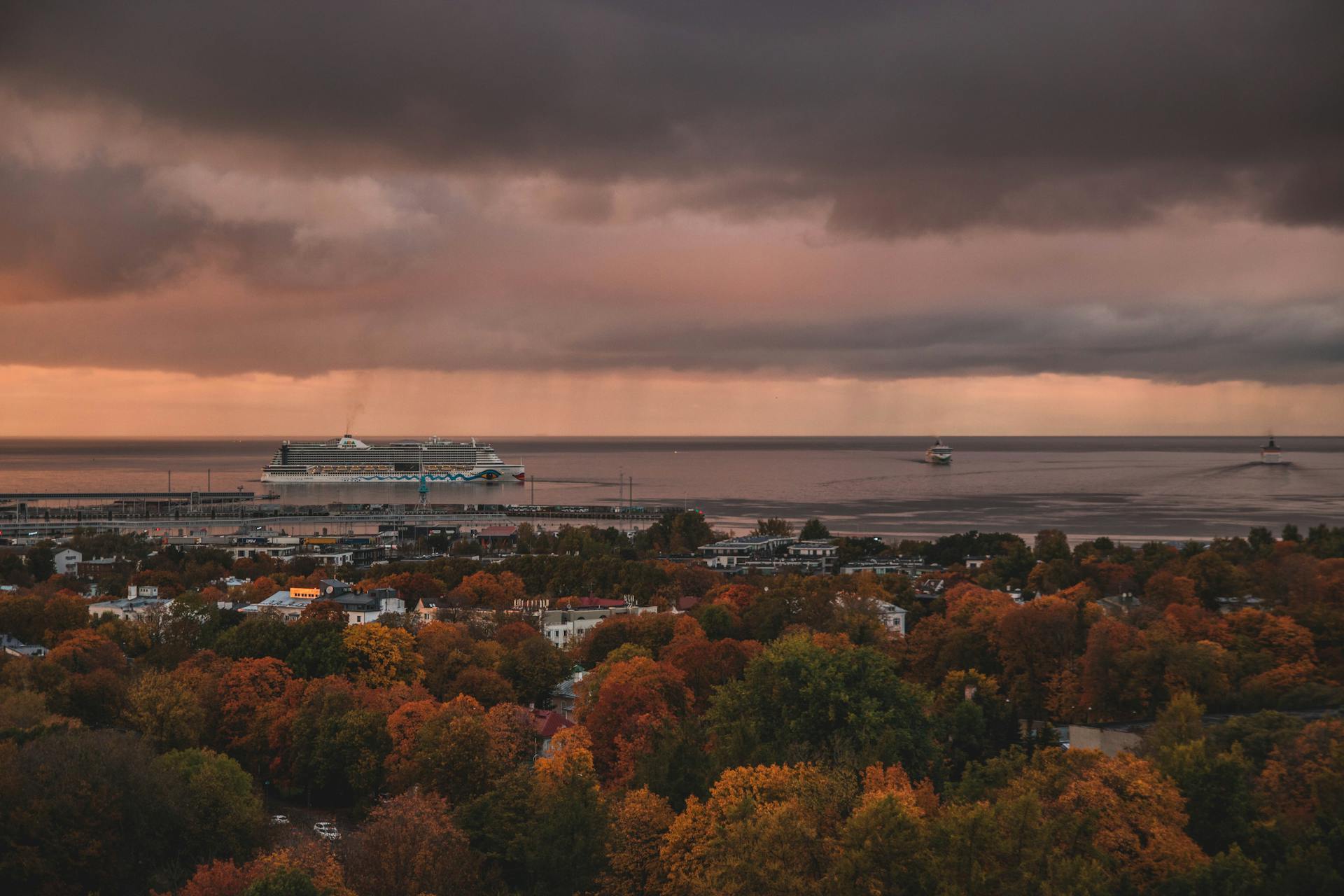 A captivating view of a harbor at sunset in autumn, showcasing a cruise ship on the horizon under dramatic clouds.