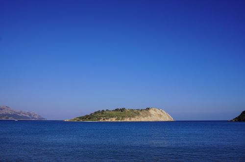 Free Tranquil view of an island surrounded by calm sea under a bright blue sky, idyllic for relaxation. Stock Photo