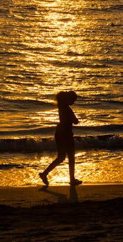 A person walking along the beach during sunset, creating a striking silhouette.