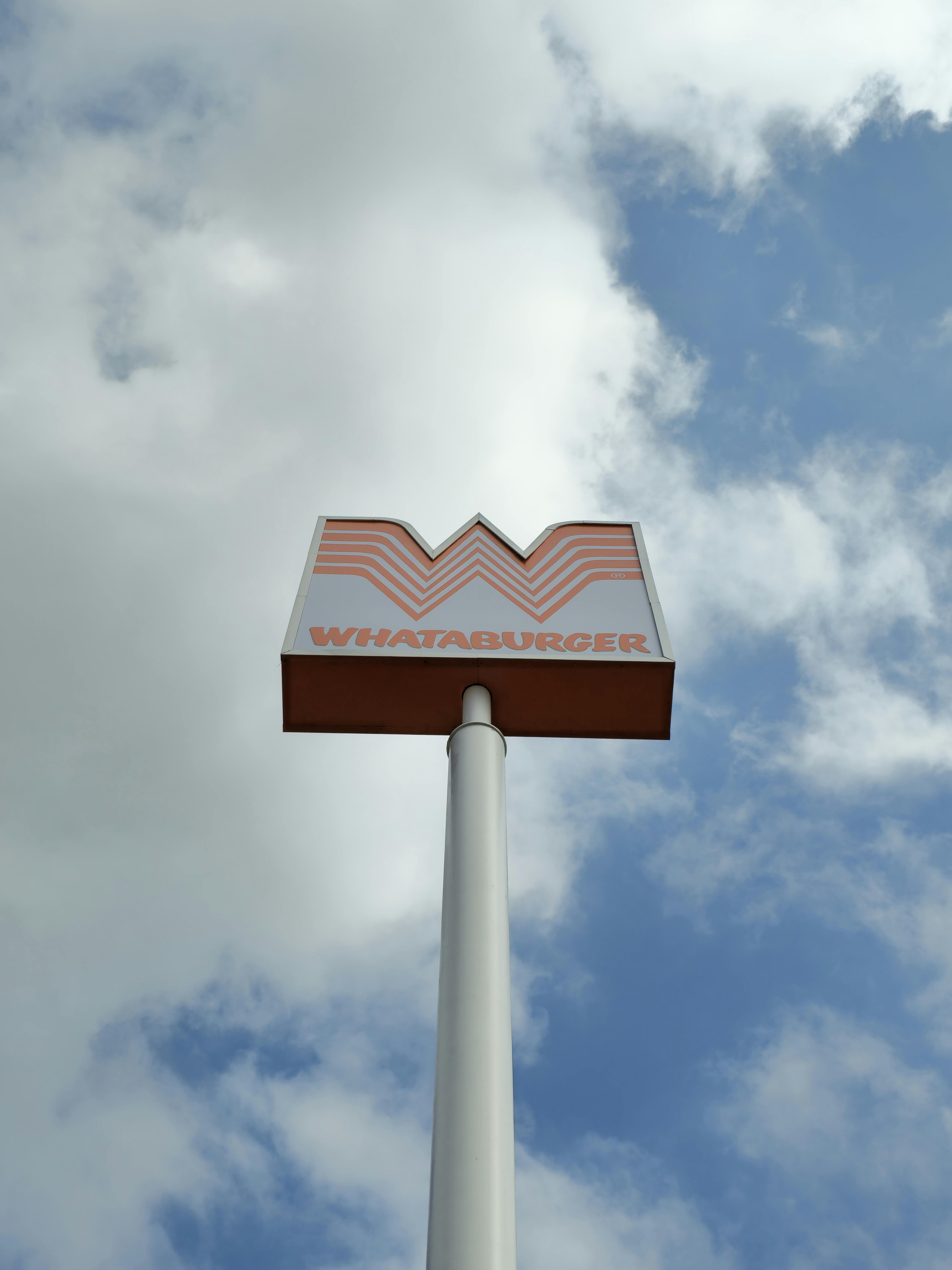 Ilmainen Korkea Whataburger-kyltti seisoo näkyvästi pilvien ja sinisen taivaan taustalla alhaalta katsottuna. Kuvapankkikuva