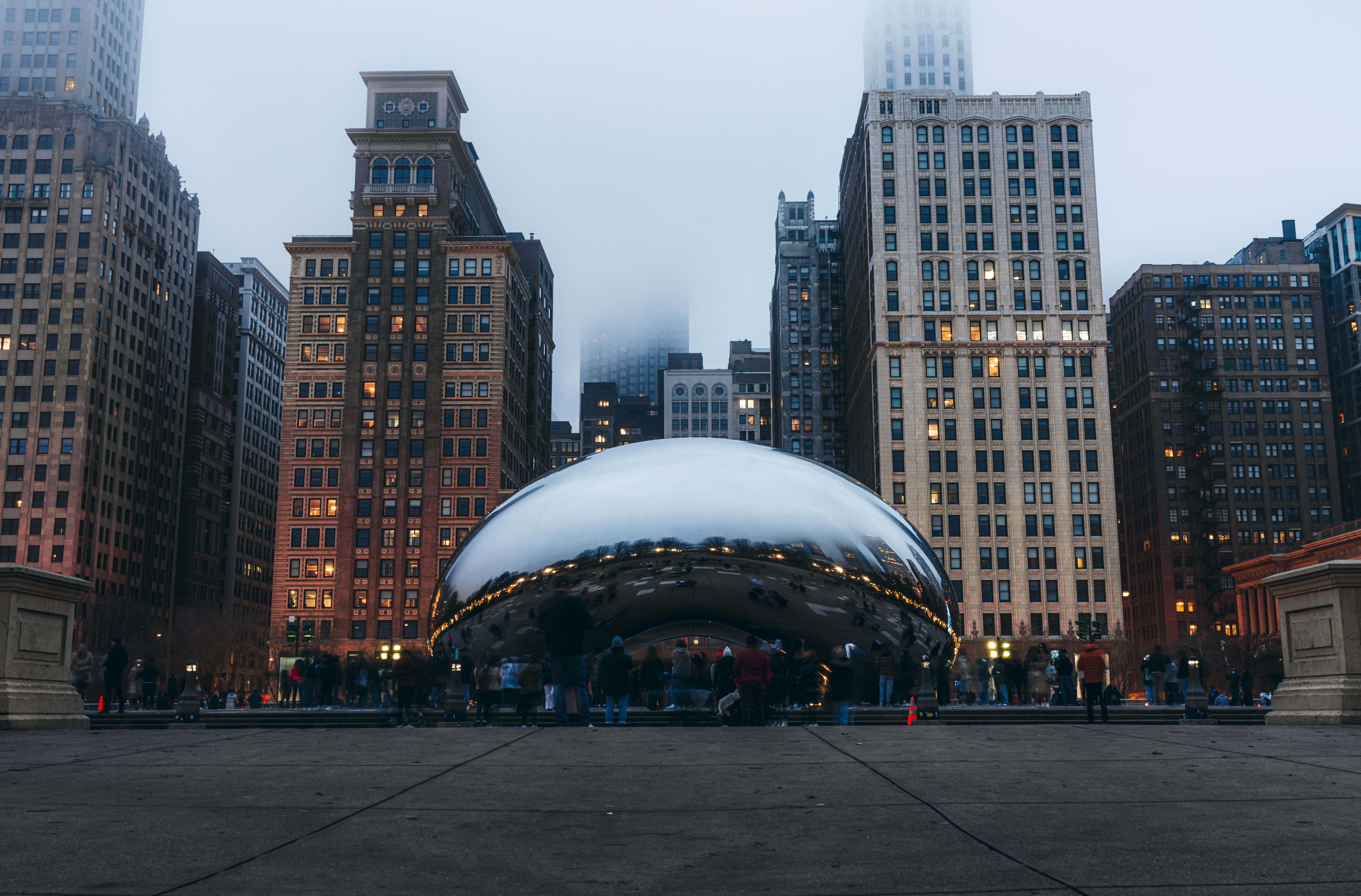 View of Cloud Gate in Chicago with skyscrapers and fog at dusk, creating a reflective urban scene.