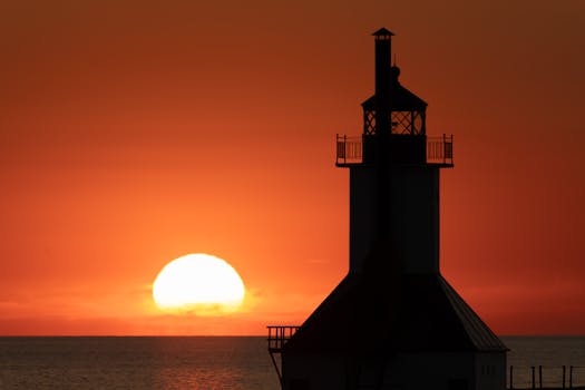 Stunning silhouette of a lighthouse against a dramatic orange sunset over the ocean.