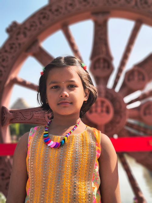 Free A young girl stands before a traditional stone wheel, wearing vibrant traditional clothing. Stock Photo