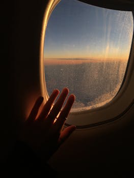 Hand on frosted airplane window with a beautiful sunrise view, exuding a sense of adventure.