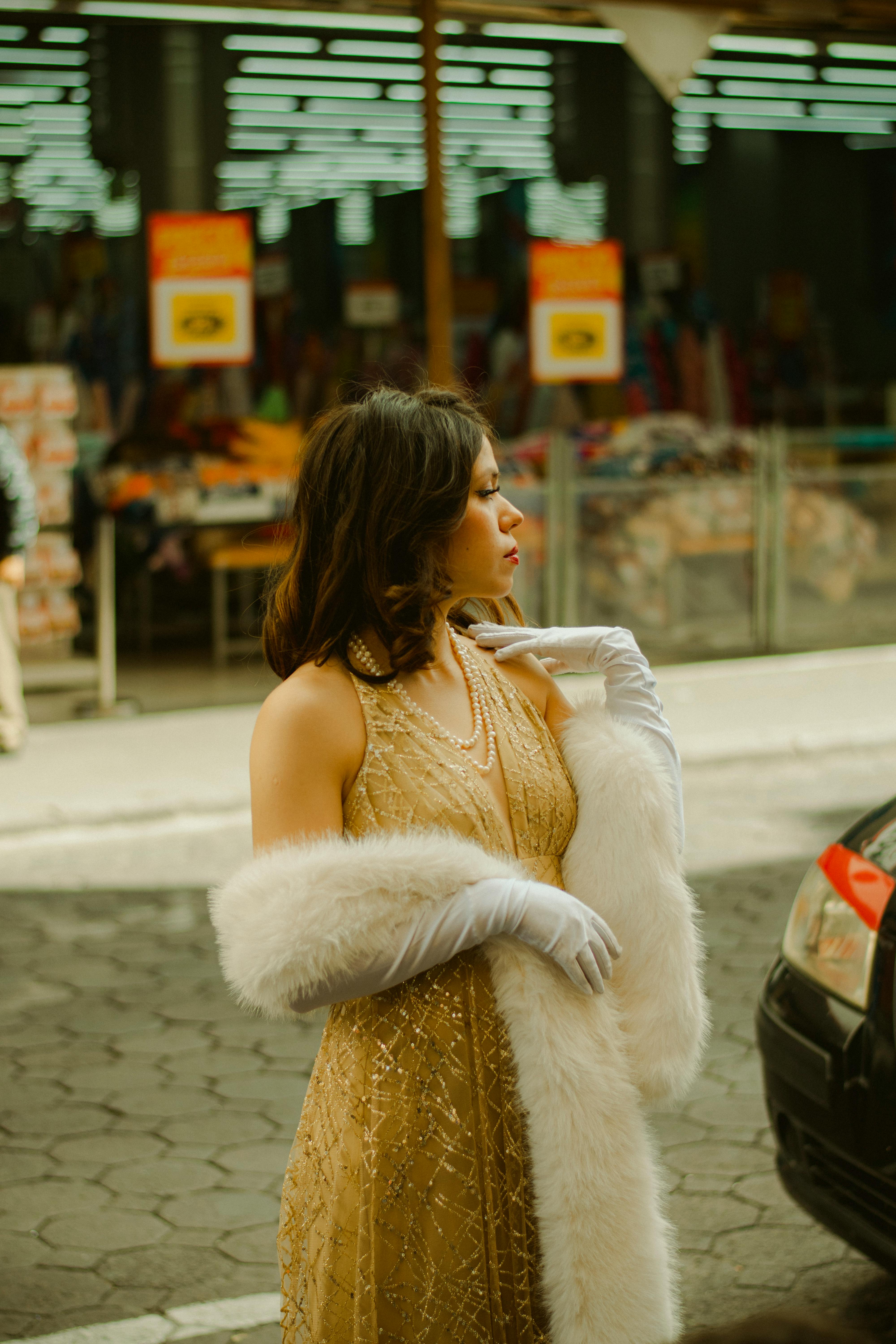 A stylish woman in a vintage gown and accessories stands confidently on a bustling city street.