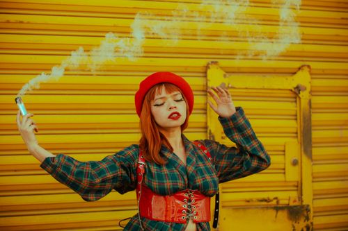 Free Stylish woman with red hat and vape against a vibrant yellow background. Stock Photo