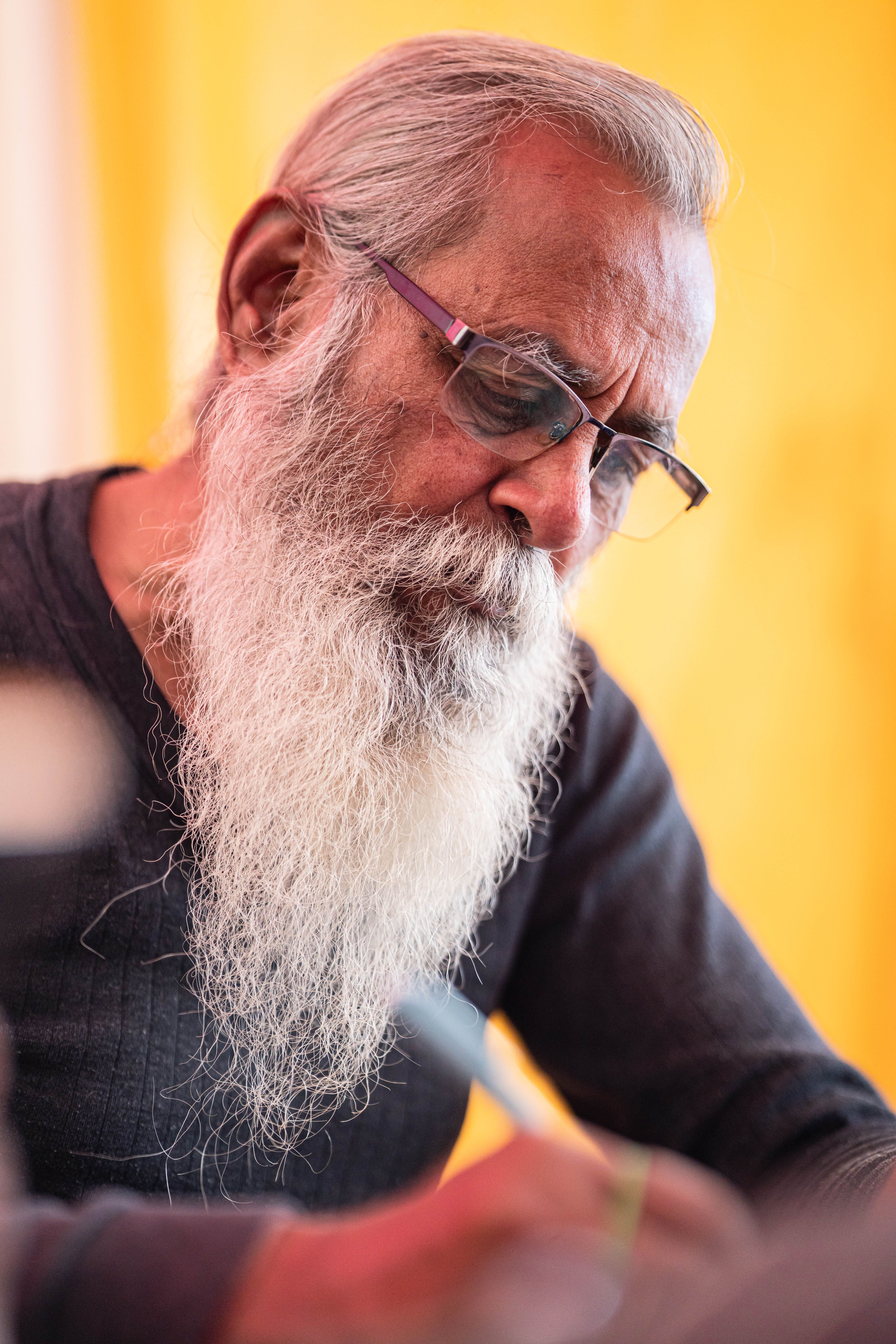 Elderly man with a long beard writes with concentration, captured in vibrant tones.