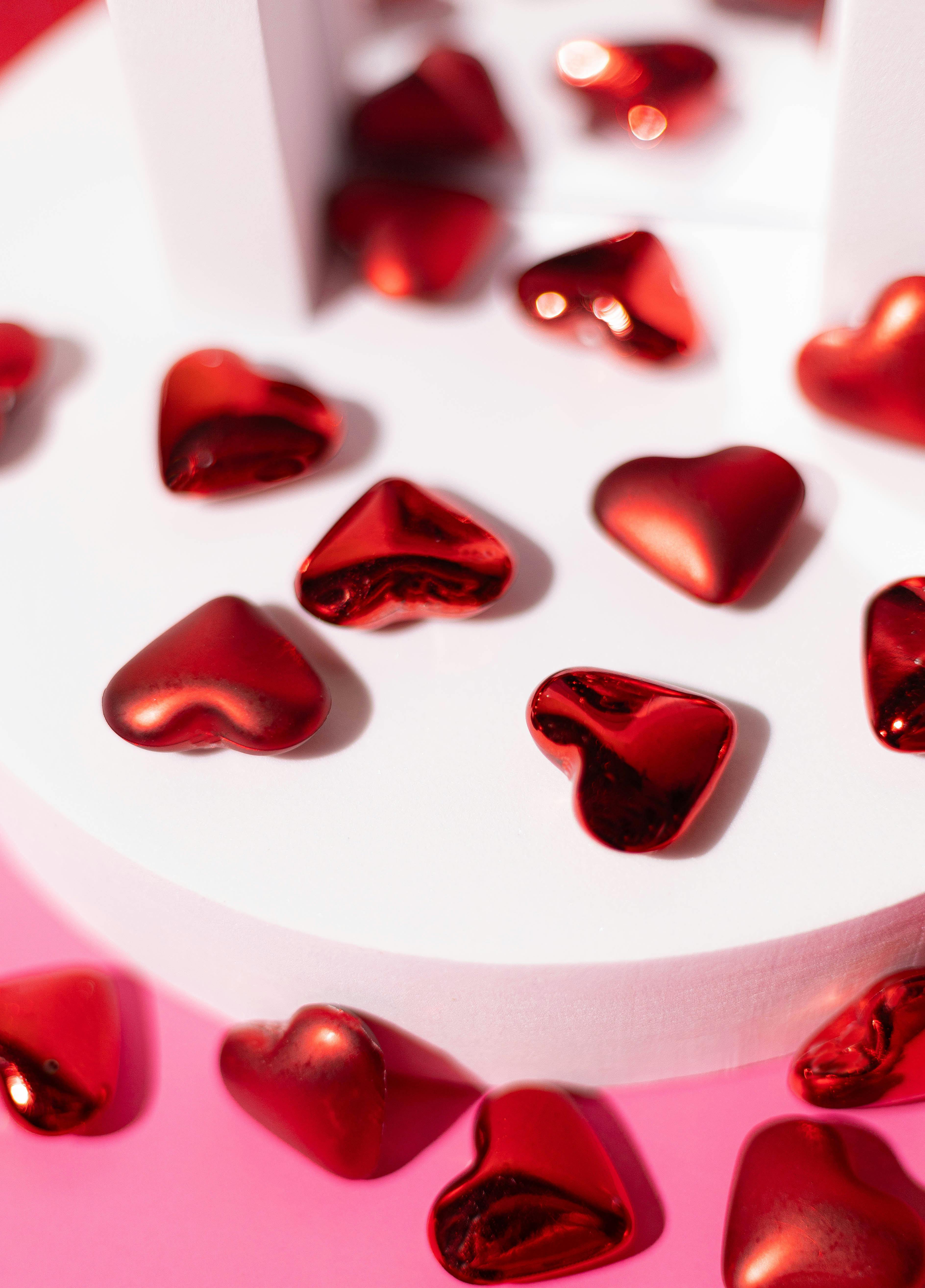Heart-shaped red chocolates scattered on a pink surface, creating a romantic and festive ambiance.