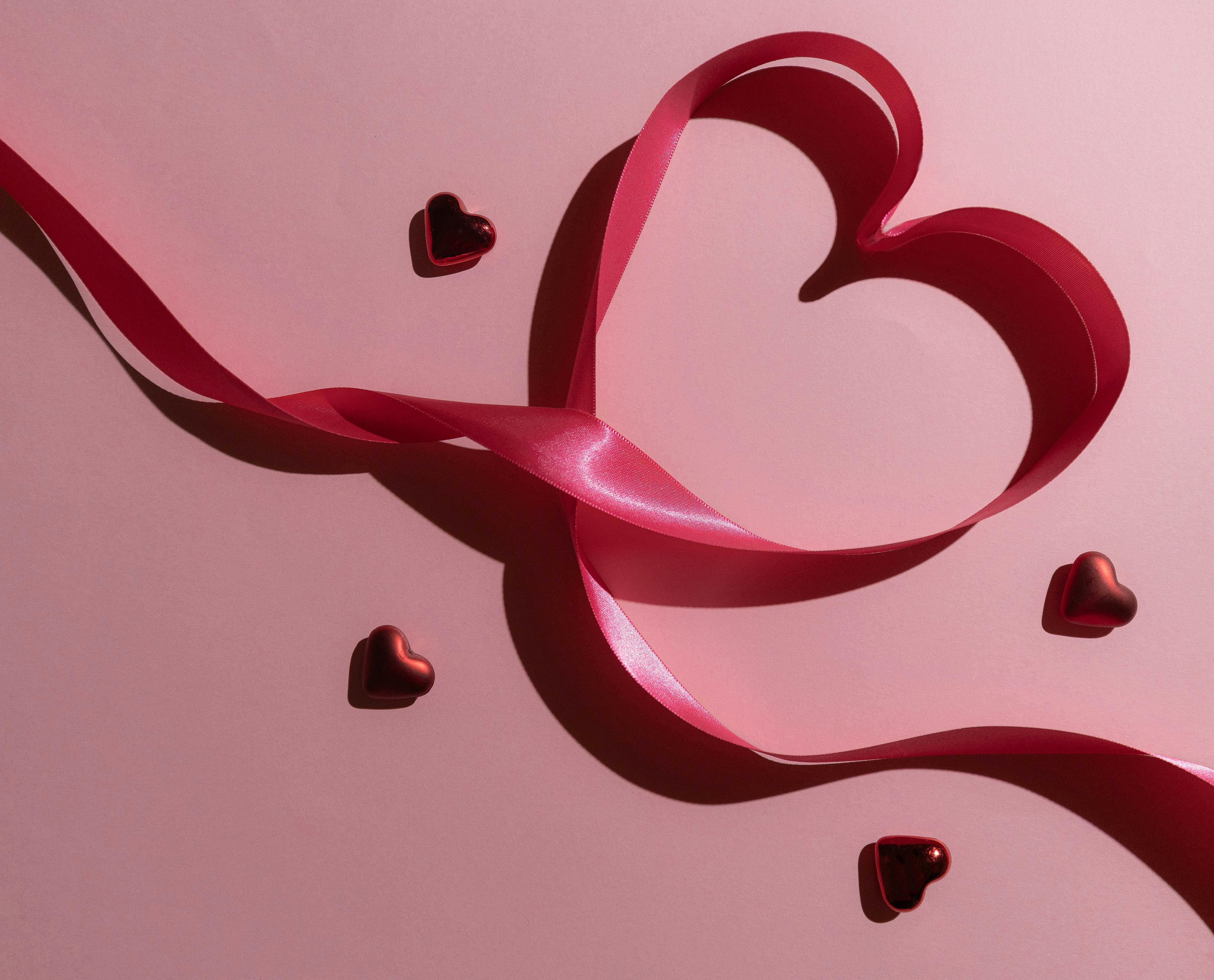 A heart-shaped red ribbon with tiny heart decorations on a pink surface, perfect for Valentine's themes.