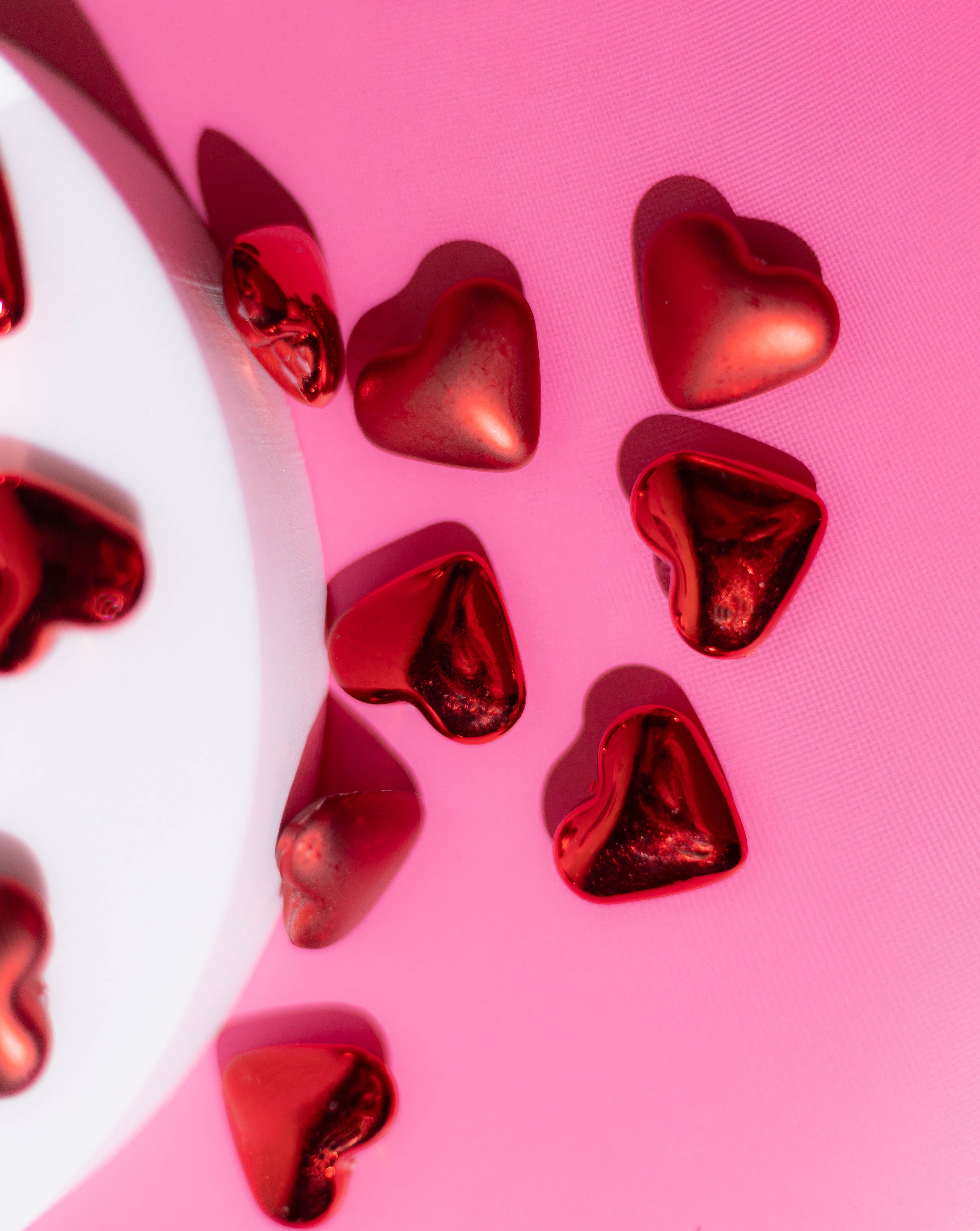 Romantic heart-shaped chocolates scattered on a vibrant pink surface, perfect for Valentine's Day.