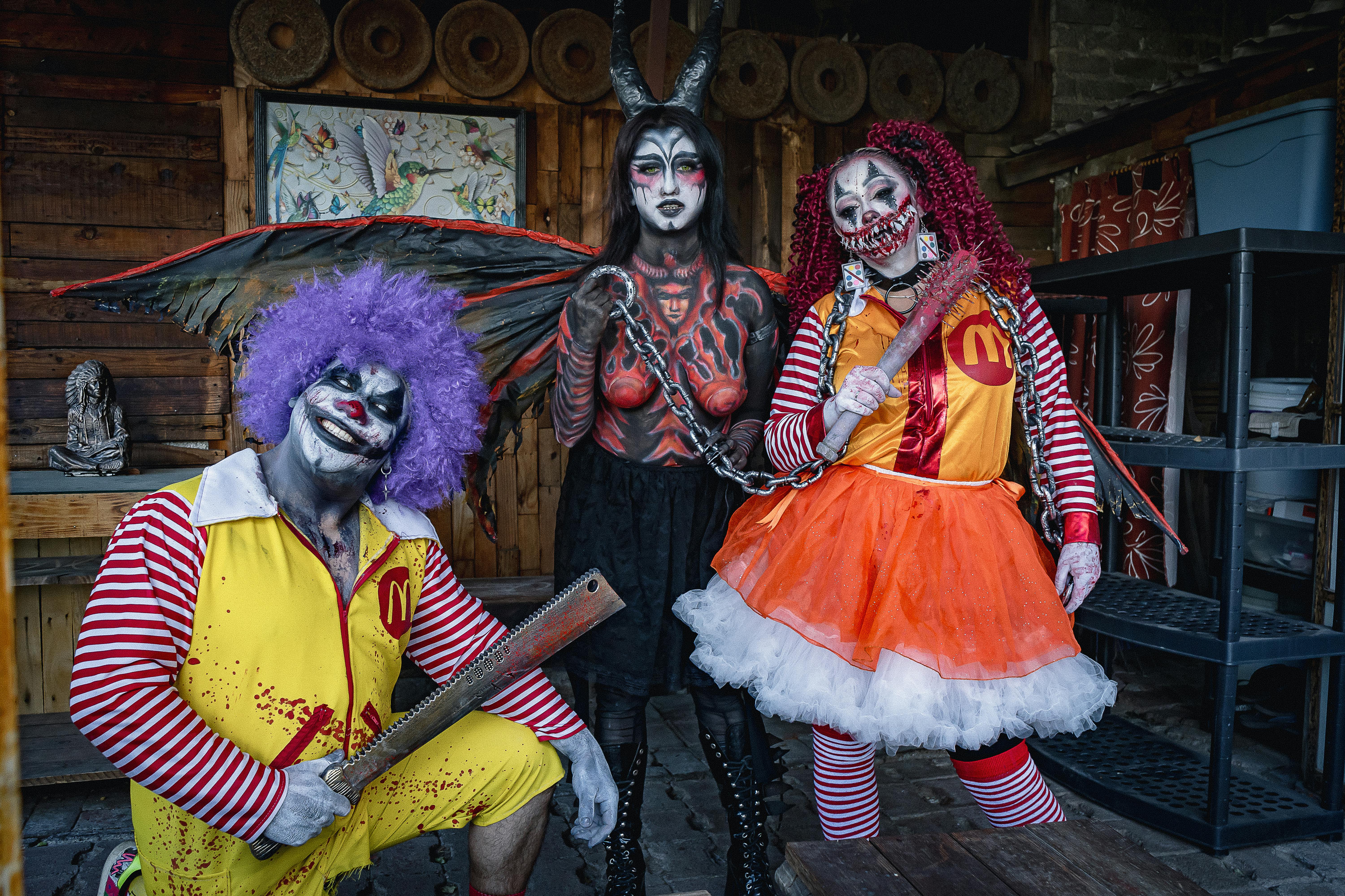 Three people in scary costumes and horror makeup pose with props indoors.