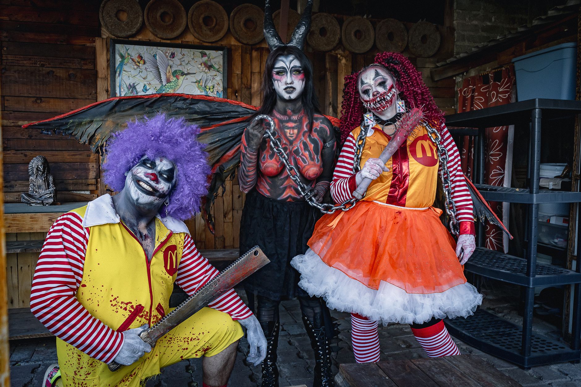 Three people in scary costumes and horror makeup pose with props indoors.