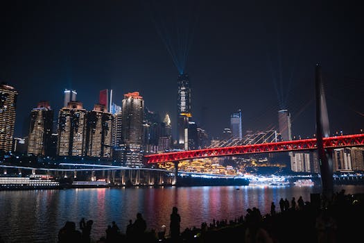 Vibrant night view of Chongqing's skyline and illuminated bridge reflecting on the river.
