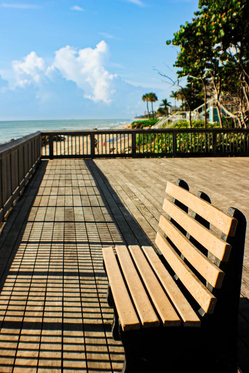 Free Peaceful boardwalk scene with a bench overlooking ocean waves and blue skies. Stock Photo