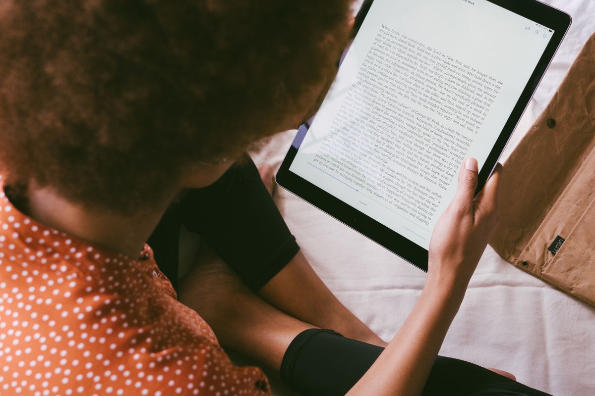 Mulher lendo um livro digital em um tablet, com uma sacola de compras ao lado, representando a conveniência da livraria online