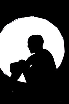 Dramatic silhouette of a person sitting against a bright circular background.