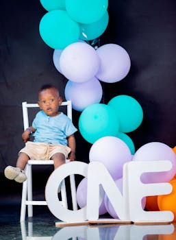 Cute baby sitting with balloons and 'ONE' sign, perfect for birthdays.
