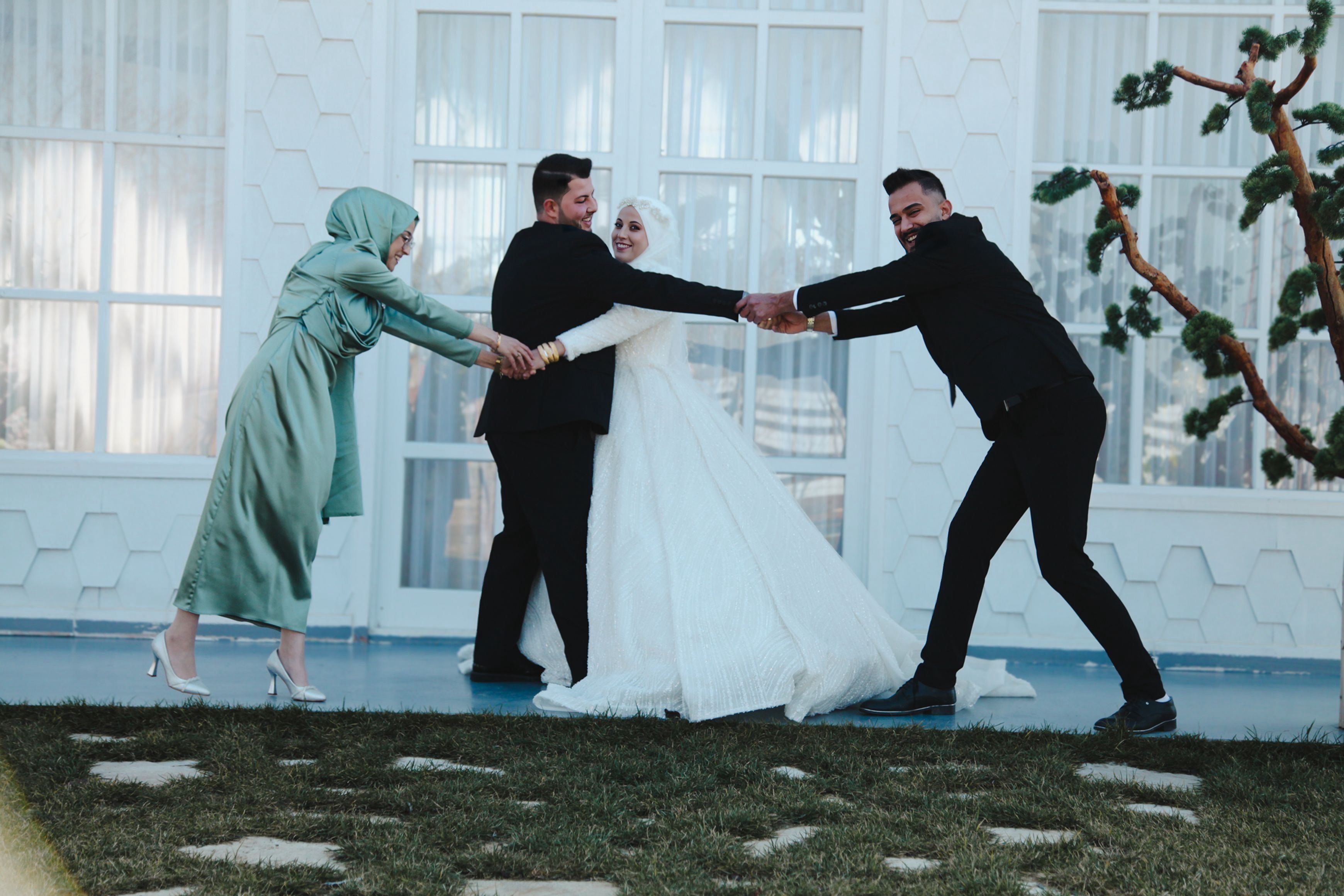 Bride and groom play tug-of-war with wedding party in a fun outdoor setting. Lively moment captured.