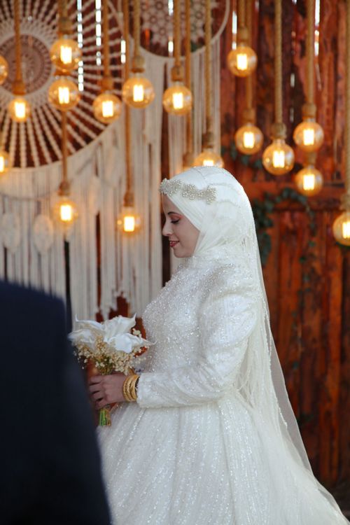Free Bride in traditional white dress holding bouquet with warm lighting and decor. Stock Photo