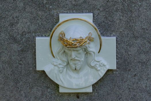 Porcelain relief depicting Jesus with a golden crown of thorns set against a stone background.