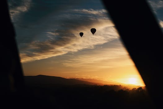 Hot air balloons float over a serene landscape at sunrise, creating a tranquil scene.
