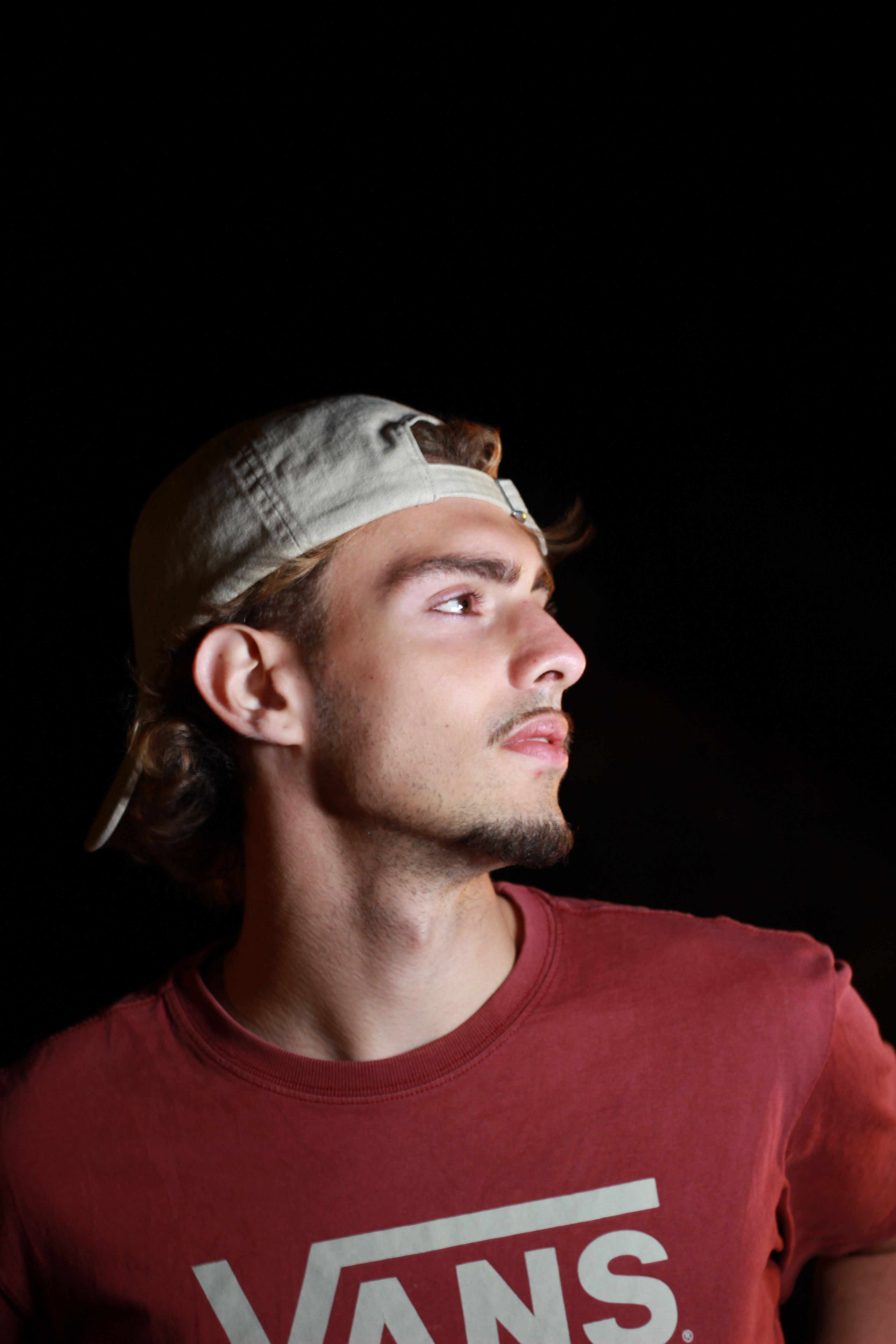 A young man with a cap gazes into the distance at night, set against a dark background.