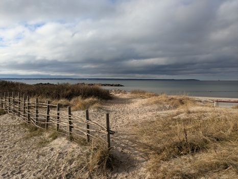 Winding sandy pathway leading to the calm sea under dramatic cloudy skies.