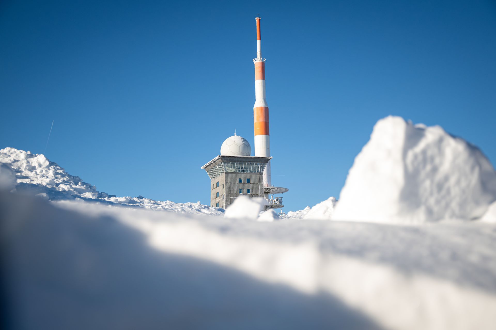 Winter view of a snowy radio tower on a mountain peak in Wernigerode, Germany, against a clear blue sky.