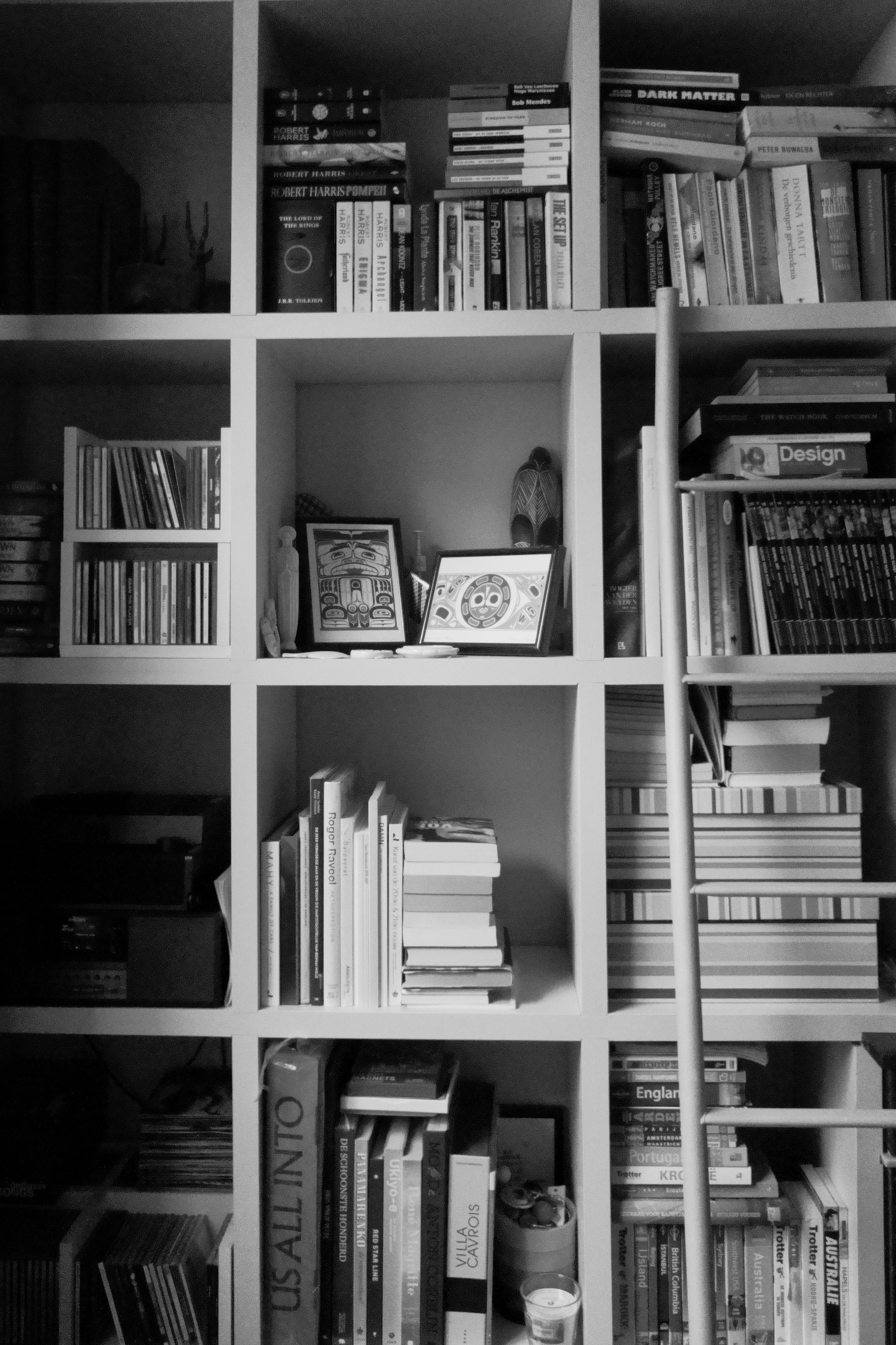 A black and white photo of an organized bookshelf with books, CDs, and decorative items.