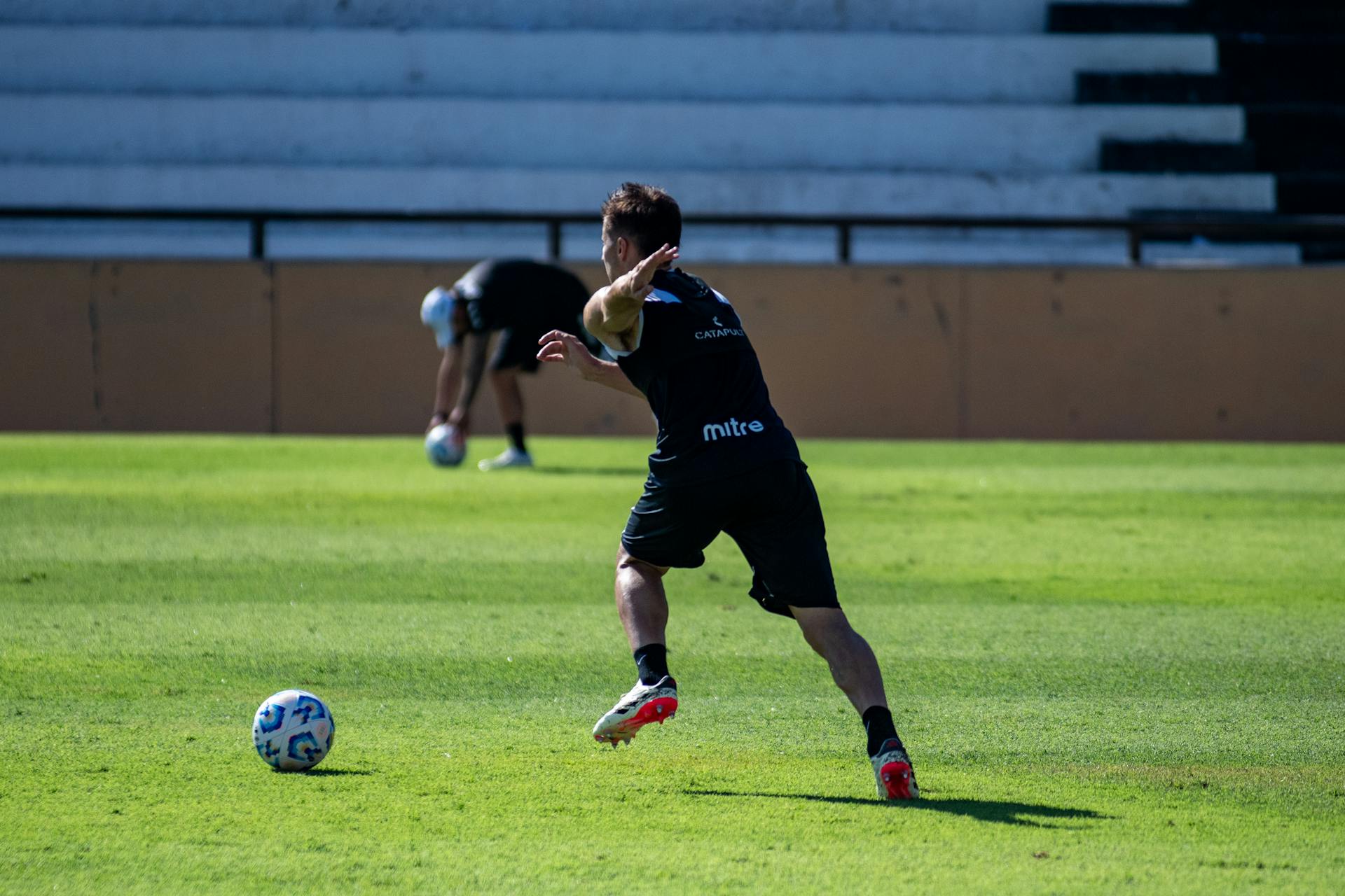 Action shot of a football player kicking the ball during training on a sunny day.