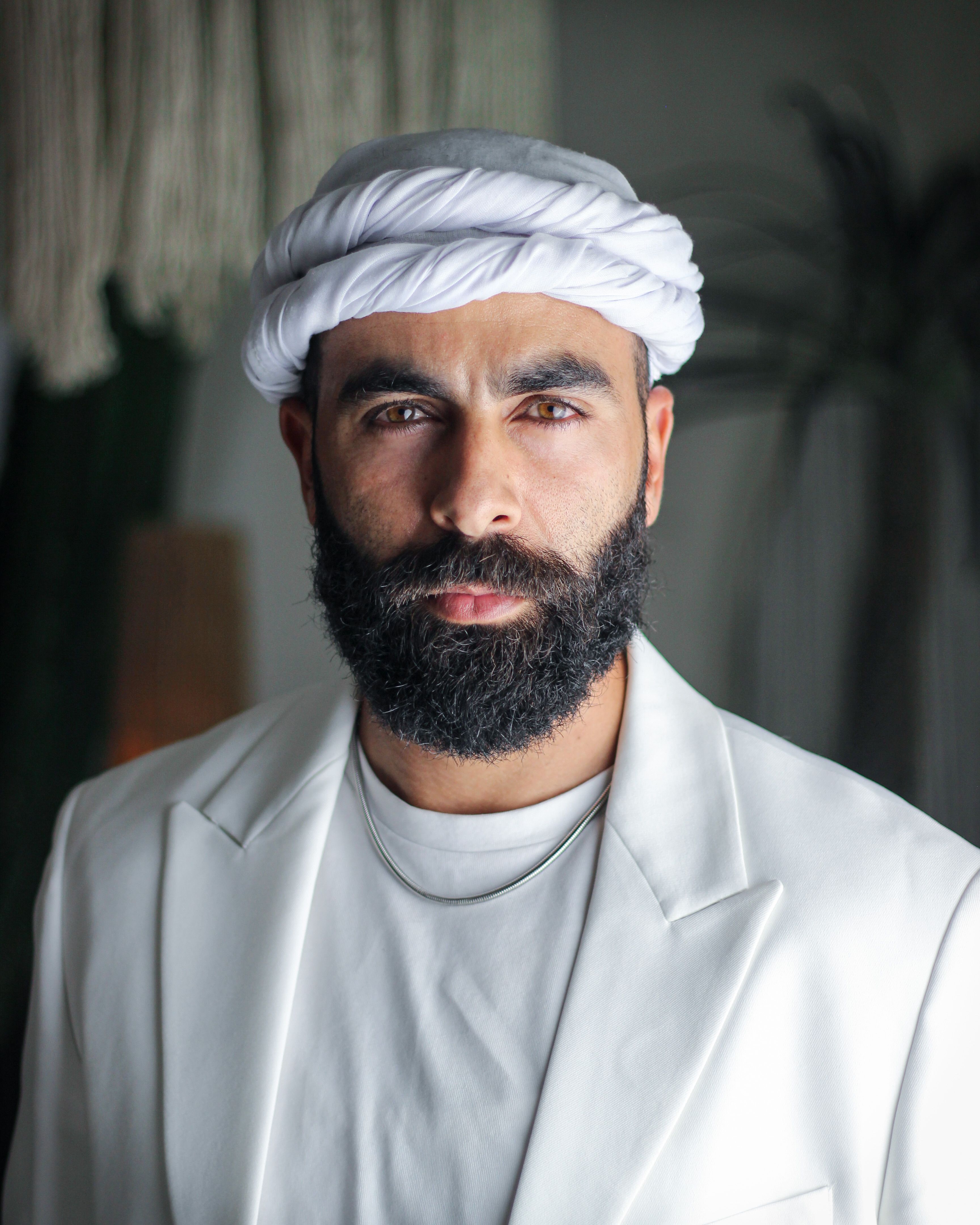 A striking portrait of a bearded man wearing traditional attire with a turban indoors.