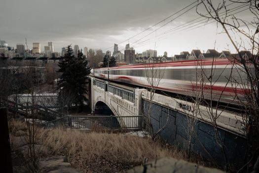 A high-speed train speeding across a bridge in Calgary with city skyline in the background.