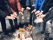 A group of people huddled together warming their hands over an outdoor fire during winter.
