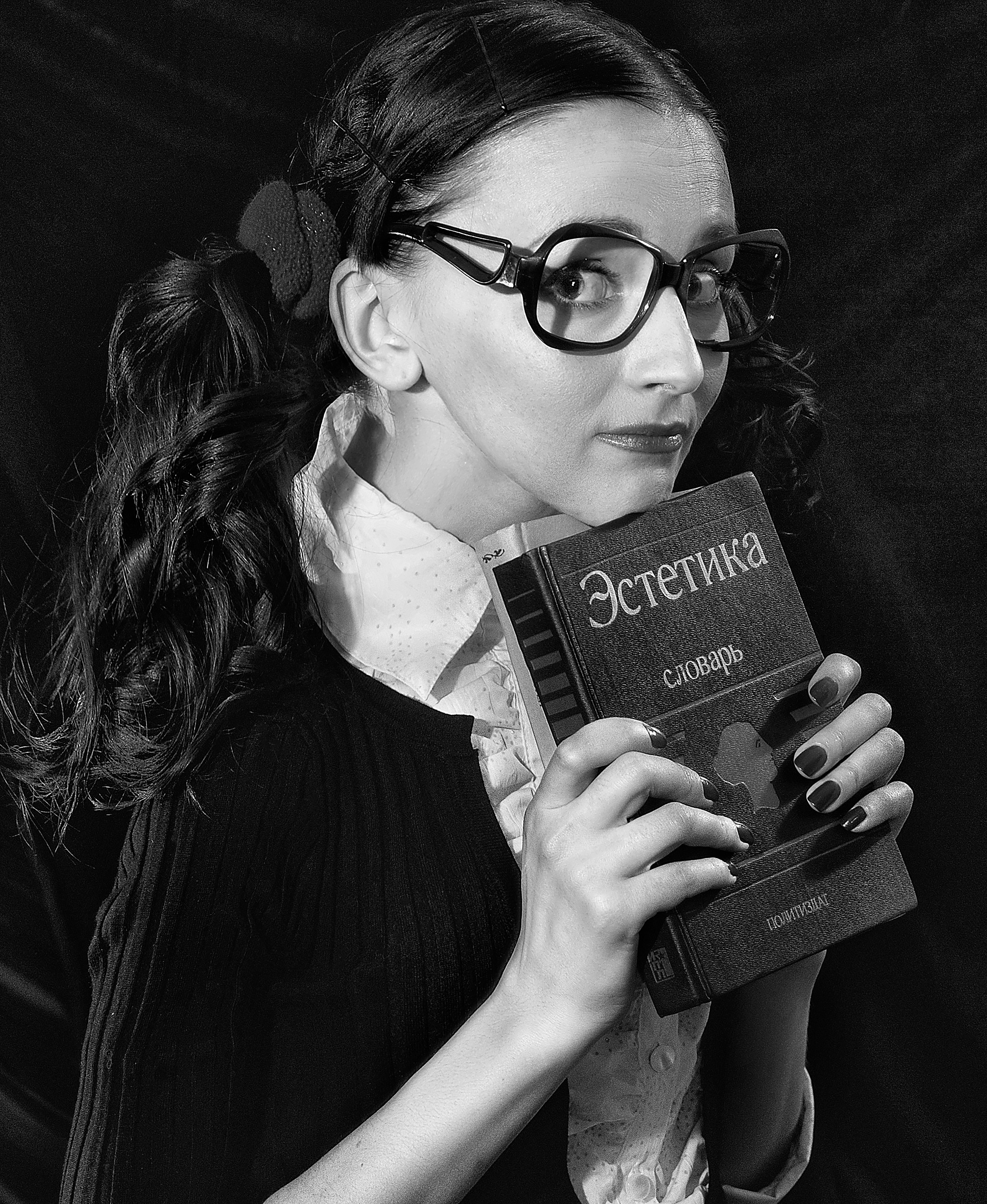 Stylish woman in glasses holding a book in a classic black and white portrait.
